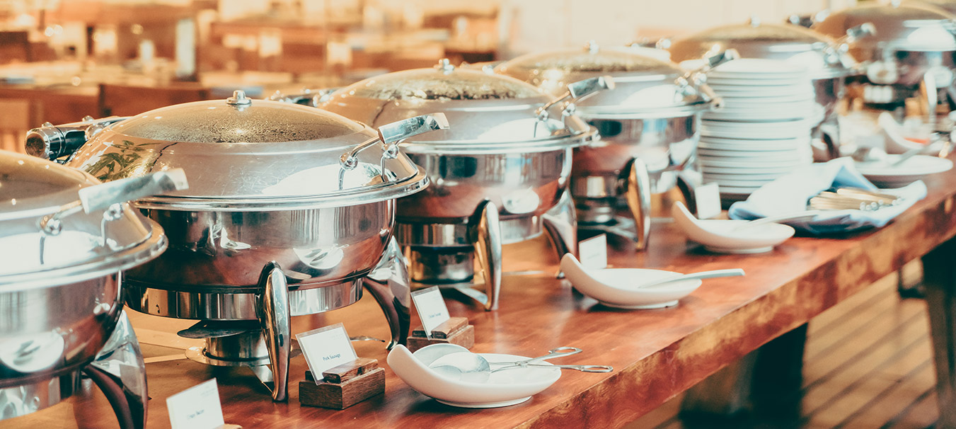 Catering setup with chafing dishes, serving spoons and stacked plates