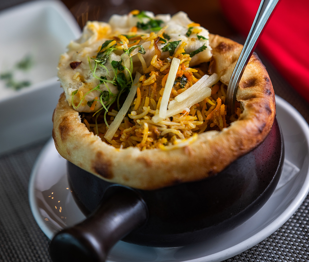 Dum biryani served in a clay pot sealed with naan, with a side of raita