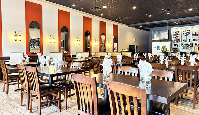 Dining tables with folded napkins beneath arched mirrors at Bombay Grove