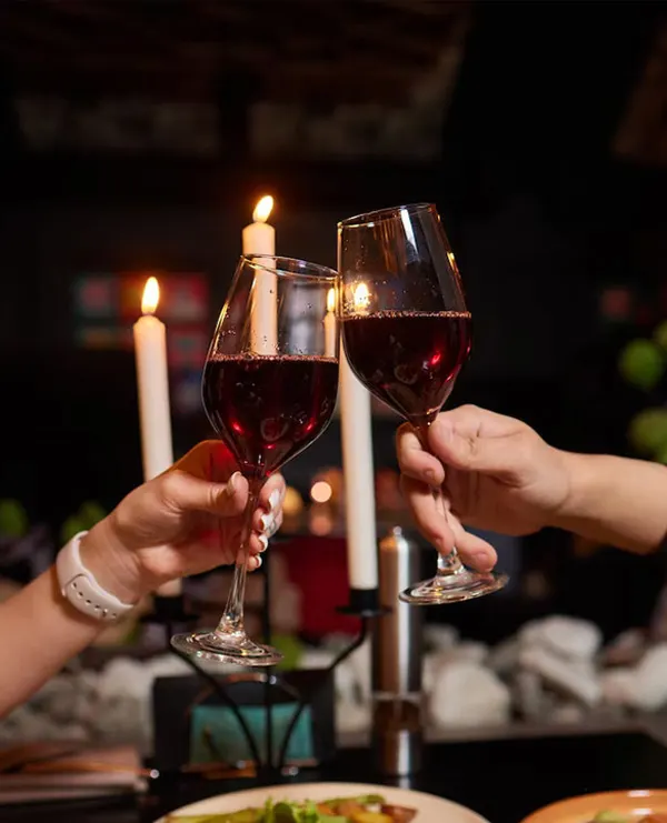 Two guests toasting with glasses of red wine by candlelight at Bombay Grove
